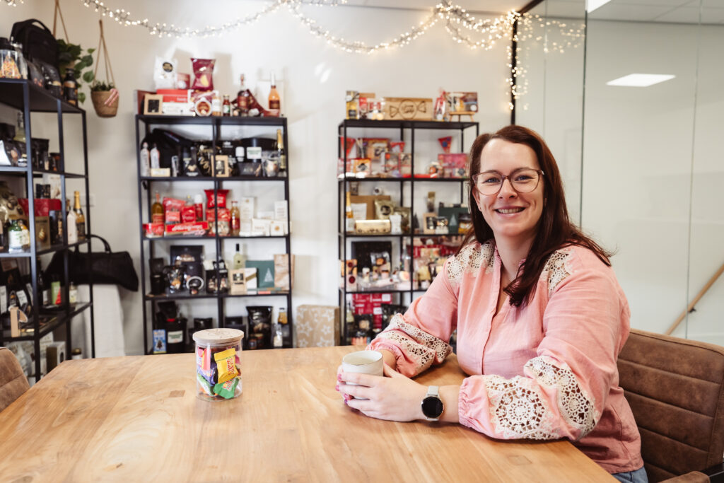 Ellen van Dijk - Vinke aan tafel in de showroom, met kasten vol originele relatiegeschenken achter haar
